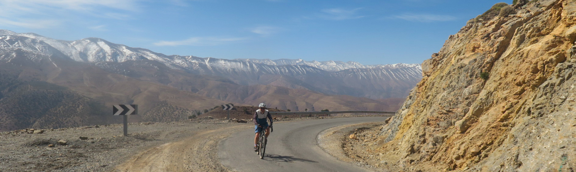 Hombre en bicicleta de gravel subiendo un puerto por una pequeña carretera de montaña en el Atlas marroquí.