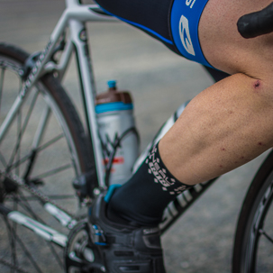 foto ciclista de carrretera, su pierna musculosa, su equipqmiento ciclista y su bici