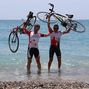 foto de fin de viaje en bici de carretera con los pies en el mediterráneo y la bici levantada como trofeo